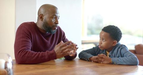 African american father and son having heartfelt conversation at sunlit wooden table