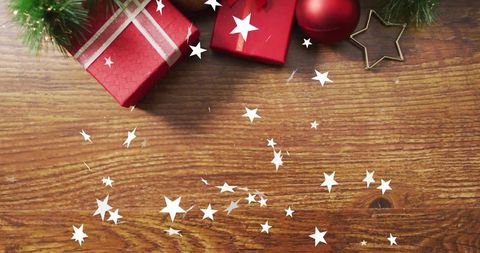 Festive red gift boxes with ribbon, baubles and gold star confetti on wooden table