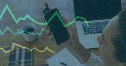 Businesswoman Tracking Stock Market on Smartphone with Laptop and Data Graphs