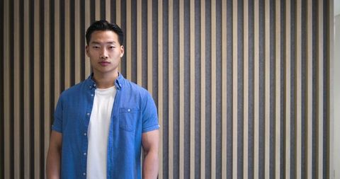Confident asian man standing by vertical wooden slat wall in modern minimal lobby