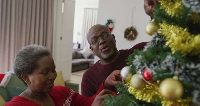 Happy senior african american couple decorating christmas tree in the living room. christmas festivities, celebrating at home.