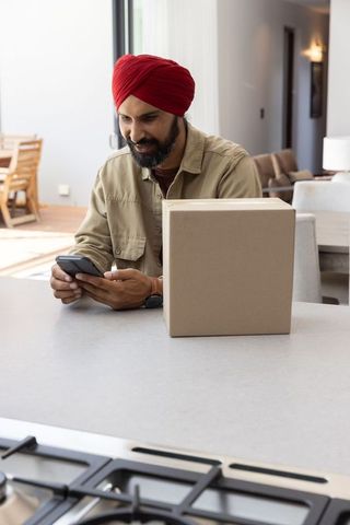 Mid adult man in turban using smartphone near package