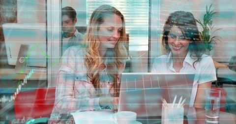 Two women collaborating on laptop with financial data overlays for business analytics