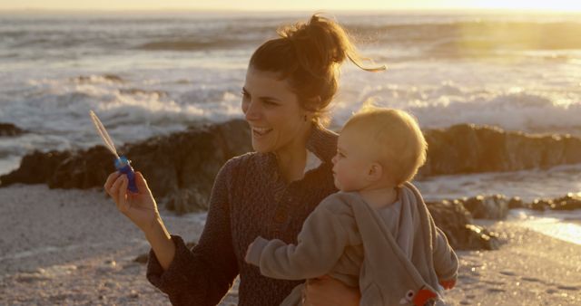 Happy caucasian mother blowing bubbles and carrying toddler son on beach at sunset - Download Free Stock Photos Pikwizard.com