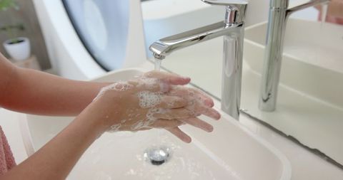 Close-up of hand washing with soap under modern faucet in minimalist bathroom
