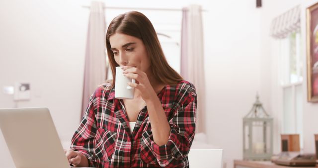 Woman Drinking Coffee While Working on Laptop in Cozy Home - Download Free Stock Images Pikwizard.com