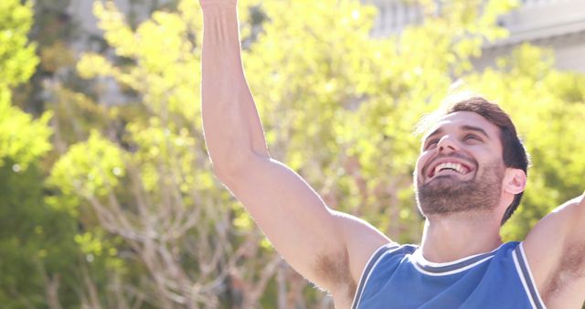 A young Caucasian man celebrates a victory or achievement outdoors, with copy space. His joyful expression and raised arm convey a sense of success and happiness.