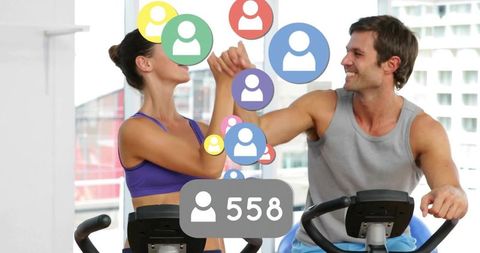 Couple exercising on stationary bikes with social media symbols