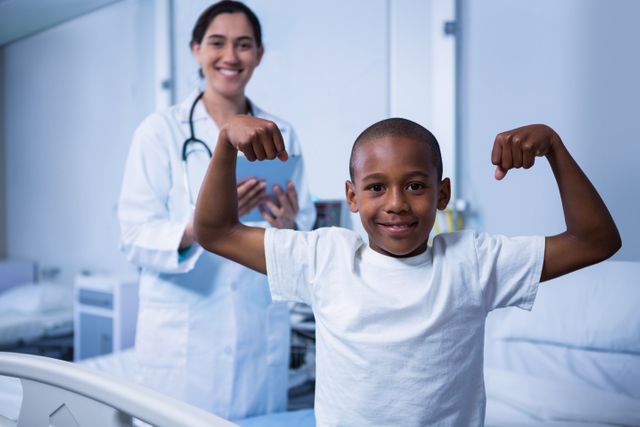 Portrait of boy flexing his muscles and female doctor standing in background in ward