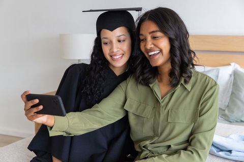 Mother and daughter taking graduation selfie on bed celebrating milestone and pride