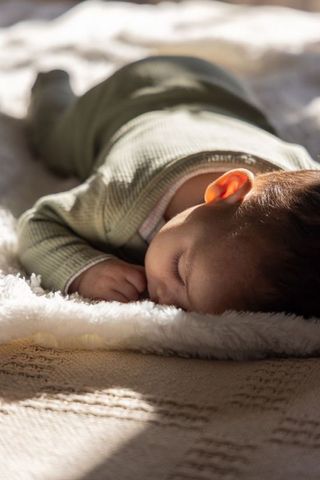 Sunlit newborn sleeping on plush faux fur blanket in green ribbed onesie