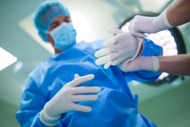 Nurse helping a surgeon in wearing surgical gloves at the hospital