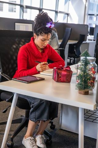 African american woman writing at decorated modern open-plan office wearing red sweater