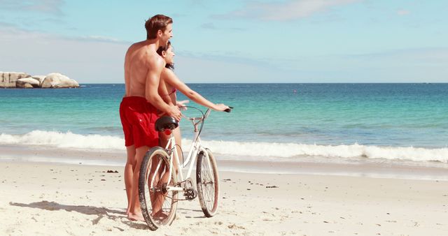 Couple enjoying a romantic bike ride on the beach shores with clear blue ocean. Ideal for use in travel promotions, summer vacation highlights, romantic getaway advertisements, or lifestyle magazines emphasizing love and fun activities.