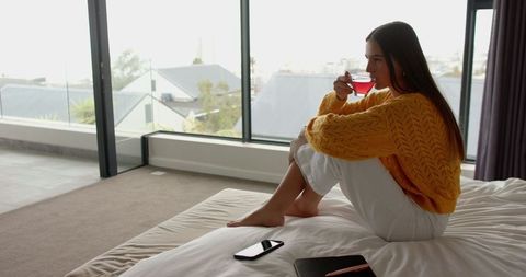 Woman Relaxing on Bed Enjoying Tea by Large Window