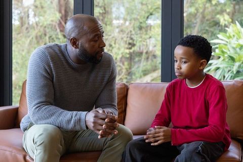 African american father having serious conversation with son on couch offering support