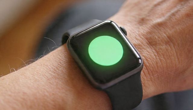 Smartwatch on left wrist showing bright green status indicator on sleek dark metal case