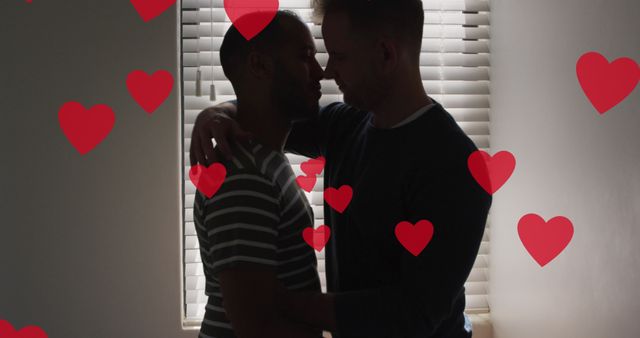 Two men embracing lovingly, standing by a window with red hearts overlay. Ideal for use in articles, advertisements, and social media posts about love, relationships, inclusivity, romance, and same-sex couples.