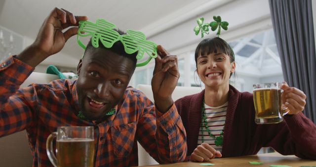 Friends enjoying St. Patrick's Day indoors wearing green costume accessories and drinking beer. Great for use in promotions for holiday events, St. Patrick's Day-themed campaigns, and festive advertisements.