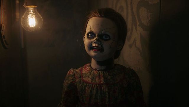 Creepy porcelain doll standing in dimly lit attic