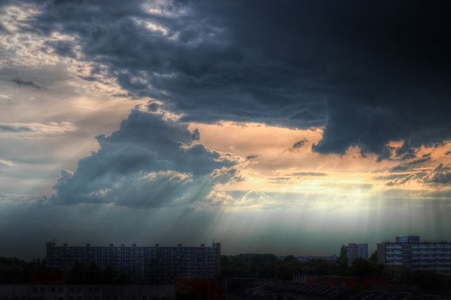 Dramatic storm clouds gather over a city skyline with buildings silhouetted against a sunset sky. This can be used for weather-related content, urban landscape features, and dramatic nature themes.