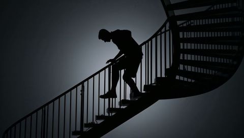 Silhouetted man climbing curved spiral staircase holding railing backlit minimalist ascent