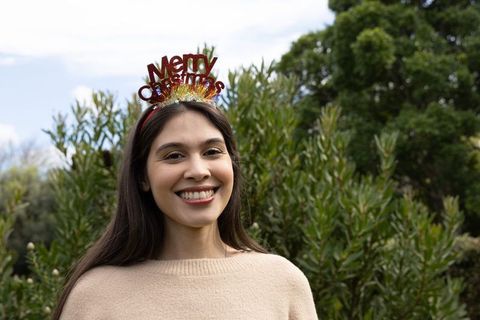 Smiling woman wearing merry christmas headband standing in green park