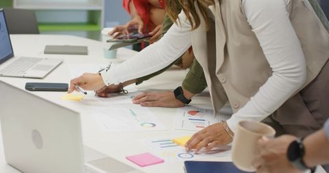 Coworkers Collaborating Over Charts, Reviewing Data, Placing Sticky Notes In Office Meeting