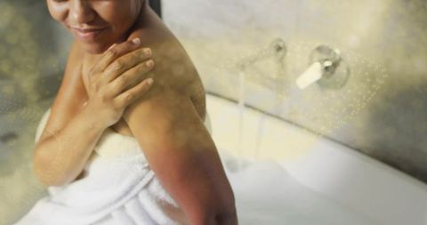 Woman wrapping towel in spa bathtub with foam and chrome faucet enjoying self-care moment