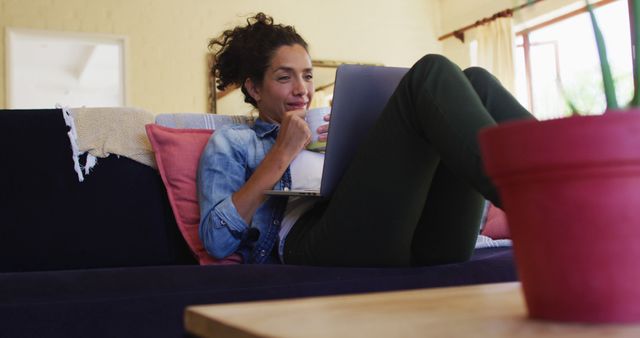 Smiling caucasian woman using laptop on image call, sitting on sofa at home. Staying at home in self isolation during quarantine lockdown.