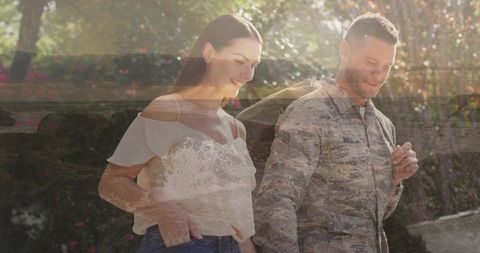Military couple walking through sunlit garden with ocean double exposure and duffel bag