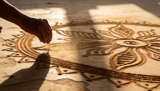 Sprinkling sand while tracing rangoli mandala on sunlit floor with dramatic shadow