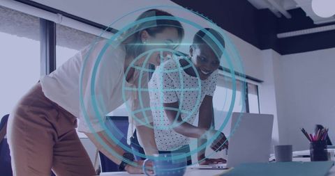 Two women collaborating over laptop with digital globe overlay in modern office workspace