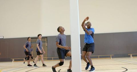 Diverse male teens spiking volleyball in indoor gymnasium during competitive team play