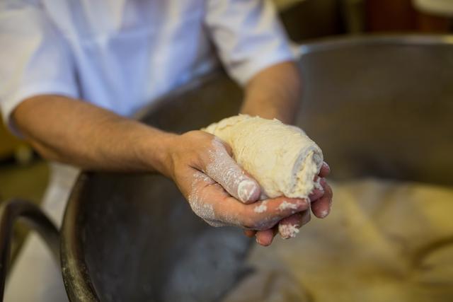 Baker holding fresh dough in hands, preparing to bake. Ideal for use in culinary blogs, bakery advertisements, cooking tutorials, and food-related articles. Highlights the artisanal process of bread making and the importance of hands-on preparation in baking.