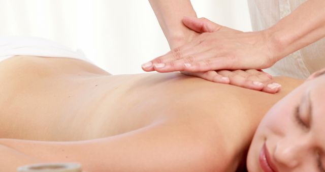 A massage therapist is performing a back massage on a young Caucasian woman, with copy space. The setting suggests a relaxing spa environment, emphasizing wellness and self-care.