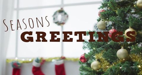 Seasons greetings text over festive christmas tree with gold baubles, tinsel and stockings