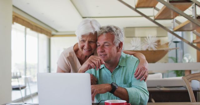 This image shows a smiling senior couple using a laptop at home, highlighting the joy and connectivity brought by modern technology. Perfect for illustrating senior lifestyle, digital communication, technology use among elderly, retirement activities, and modern family life. Ideal for blogs, advertisements, and publications related to seniors and technology, healthy aging, and home living.