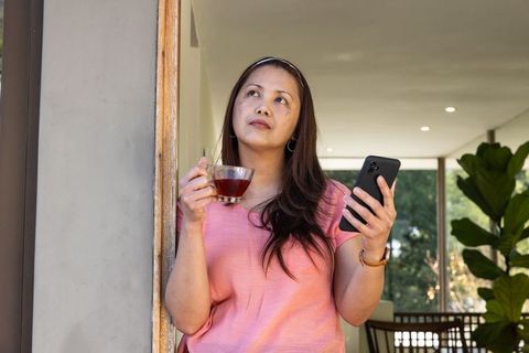 Mature Woman Contemplating with Tea and Smartphone in Modern Home