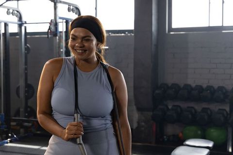 Smiling african american woman holding battle rope after strength training in urban gym