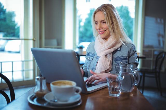 Smiling woman using laptop while having coffee in cafÃ©