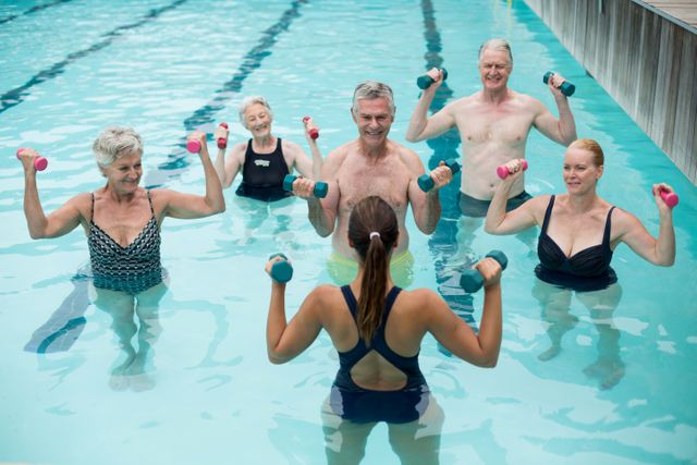 Senior individuals participating in a water aerobics class led by an instructor in a swimming pool. They are holding dumbbells and performing exercises together. This image can be used for promoting senior fitness programs, health and wellness campaigns, or aquatic exercise classes.