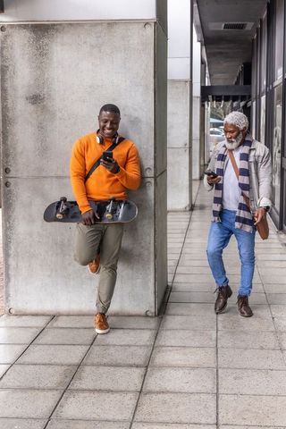 Multigenerational african american men using smartphones in urban corridor with skateboard