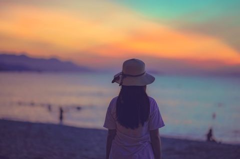 Woman in Hat Admiring Tranquil Beach Sunset