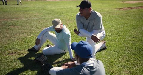 Baseball teammates resting and talking on grass infield during sunny practice session