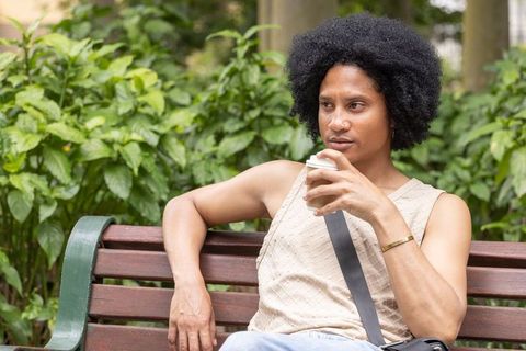 African american man relaxing on park bench sipping takeaway coffee, contemplative portrait