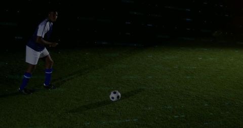 Night soccer player preparing to strike ball under spotlight on turf with copy space