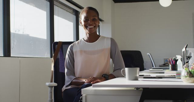Happy african american businesswoman sitting at desk and smiling at work. independent creative business at a modern office.
