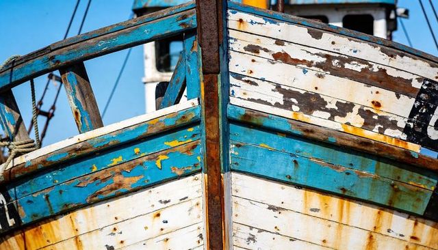 Weathered wooden fishing boat bow showing peeling paint, rust streaks, patina and corrosion