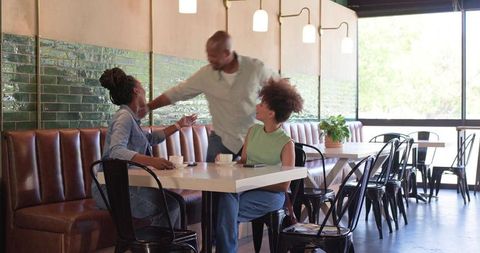 African friends greeting and chatting over coffee in sunlit modern cafe interior, smiling